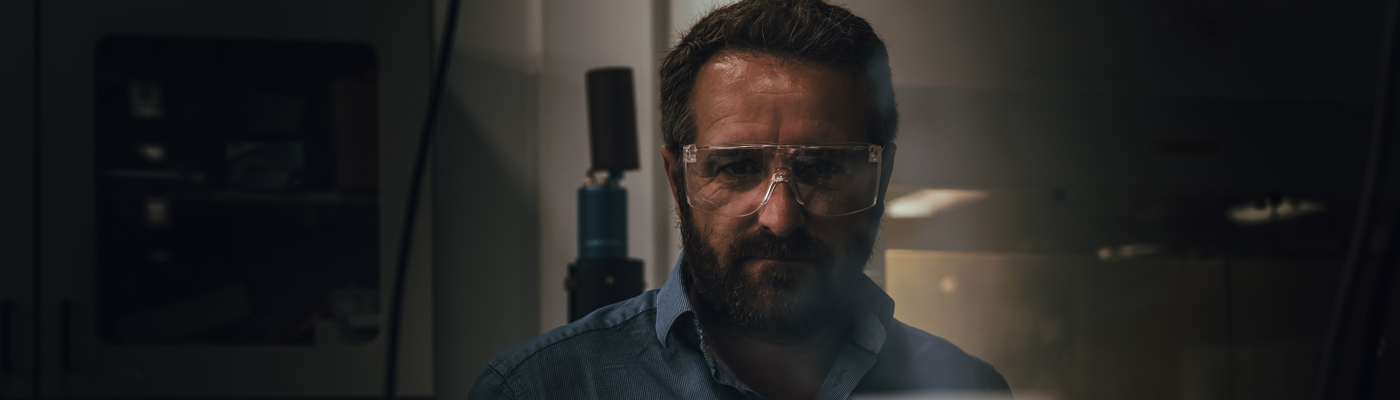 Man in goggles and blue shirt stood in dimly lit room