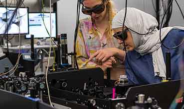 Two ladies with shaded protective glasses on peering into lab equipment